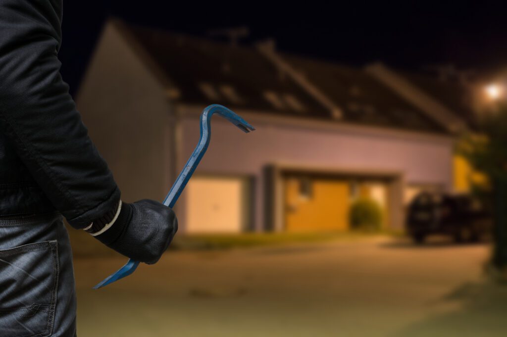 Crime concept. Burglar or robber with crowbar stands in front of the house at night.